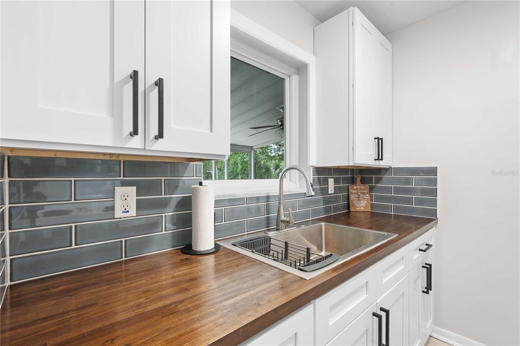 A kitchen sink area with white cabinets, a wood countertop, and a gray subway tile backsplash — 215 ABBEYVILLE STREET, DELTONA, FL