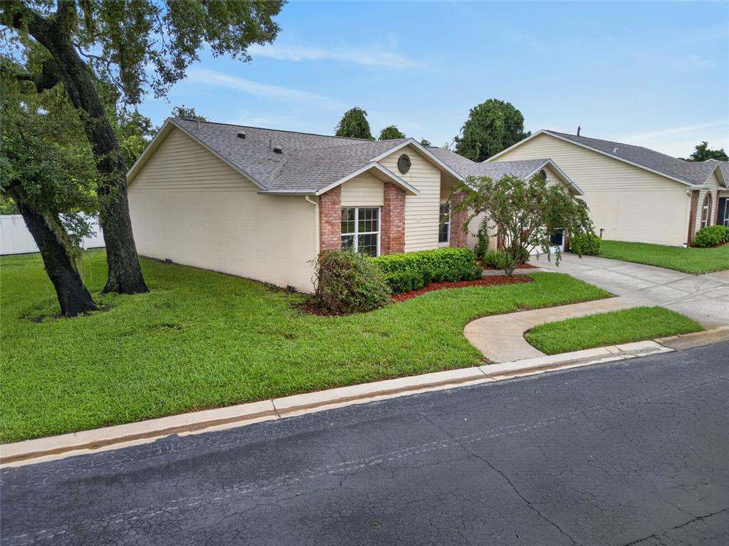 A single-story house with beige siding, brick accents, and a gray shingled roof — 4949 BOSTONIAN LOOP, NEW PORT RICHEY, FL