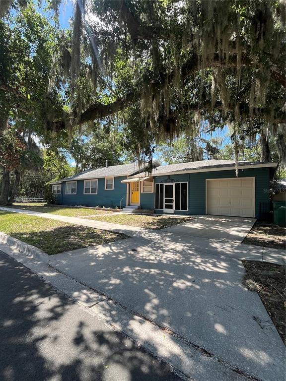 A blue single-story house with a yellow front door, a garage, and large oak trees — 949 N GRANDVIEW STREET, MOUNT DORA, FL