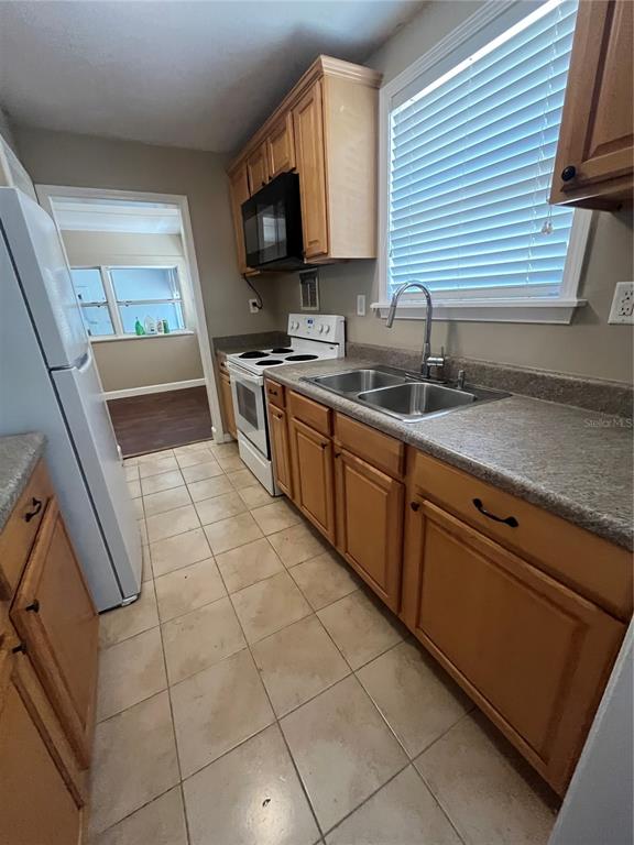 A kitchen features light wood cabinets, a white stove, a double sink, and tiled flooring — 949 N GRANDVIEW STREET, MOUNT DORA, FL