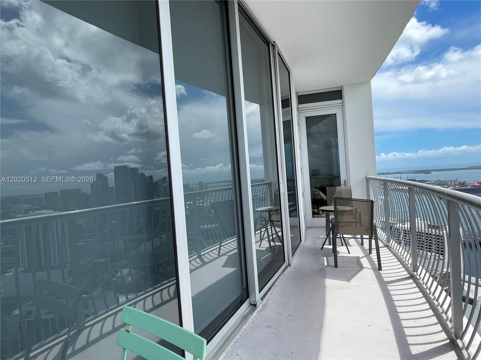 A high-rise balcony features a metal railing, glass sliding doors, and outdoor patio furniture — 1750 N Bayshore Dr # 5614, Miami FL 33132, MIAMI, FL