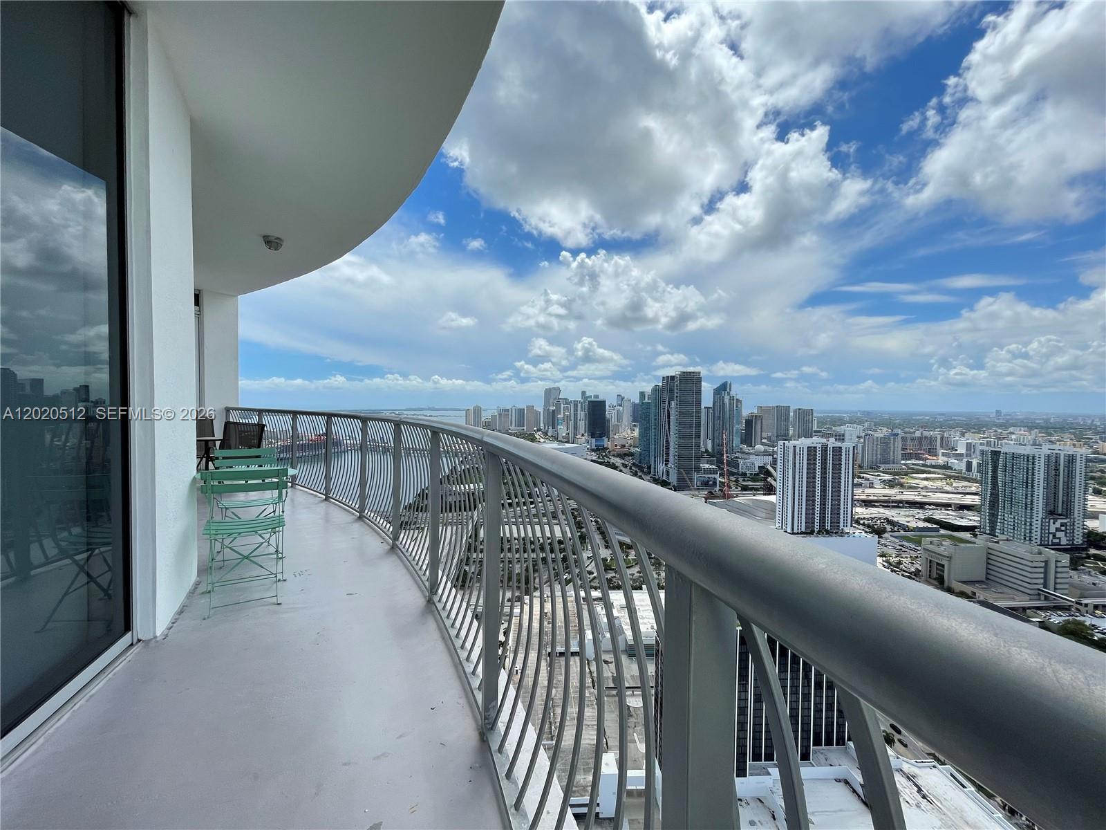 A curved balcony with metal railings overlooks a city skyline under a cloudy blue sky — 1750 N Bayshore Dr # 5614, Miami FL 33132, MIAMI, FL