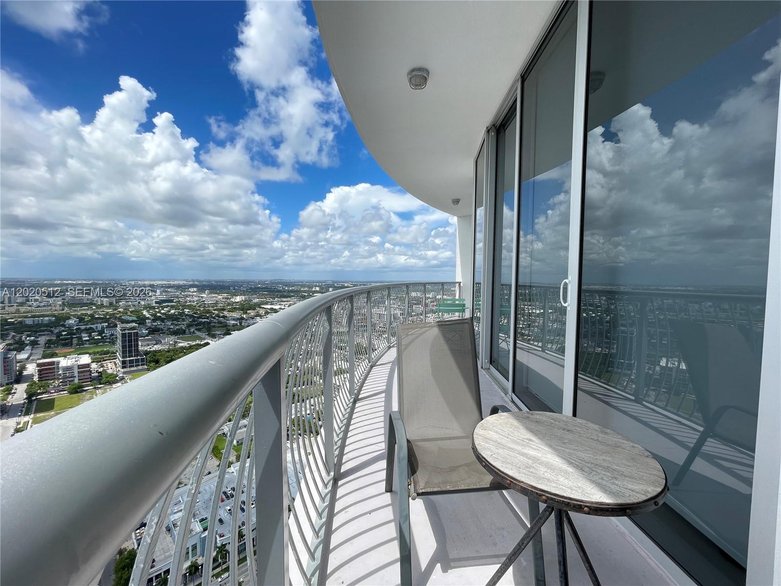 A high-rise balcony features a metal railing, a small table, and a chair overlooking a city — 1750 N Bayshore Dr # 5614, Miami FL 33132, MIAMI, FL