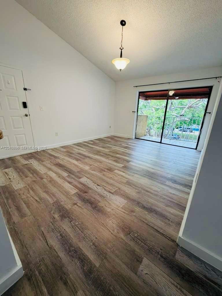 An empty room features wood-look flooring, a vaulted ceiling, a light fixture, and sliding doors — 15530 SW 80th St # 306, Miami FL 33193, MIAMI, FL