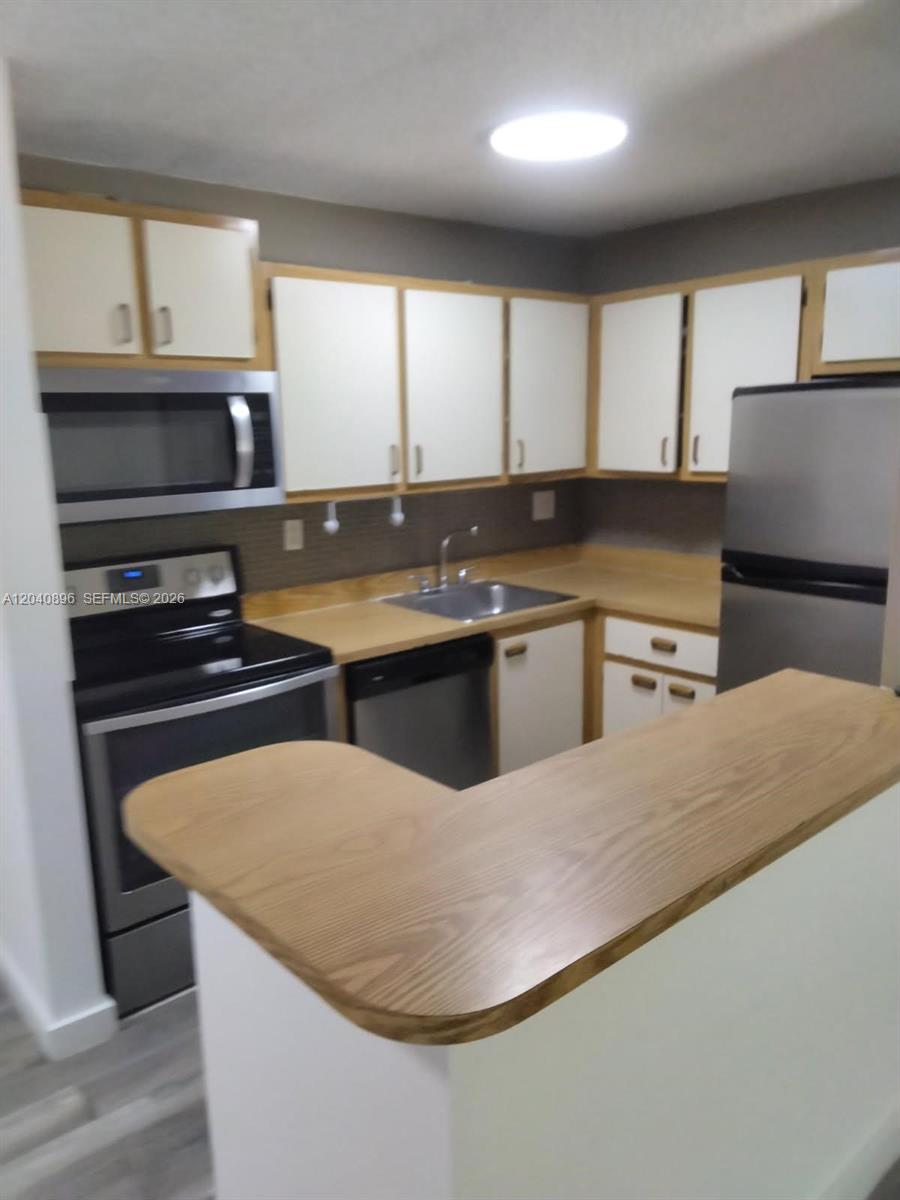 A kitchen features white cabinets with wood trim, stainless steel appliances, and a breakfast bar — 15530 SW 80th St # 306, Miami FL 33193, MIAMI, FL