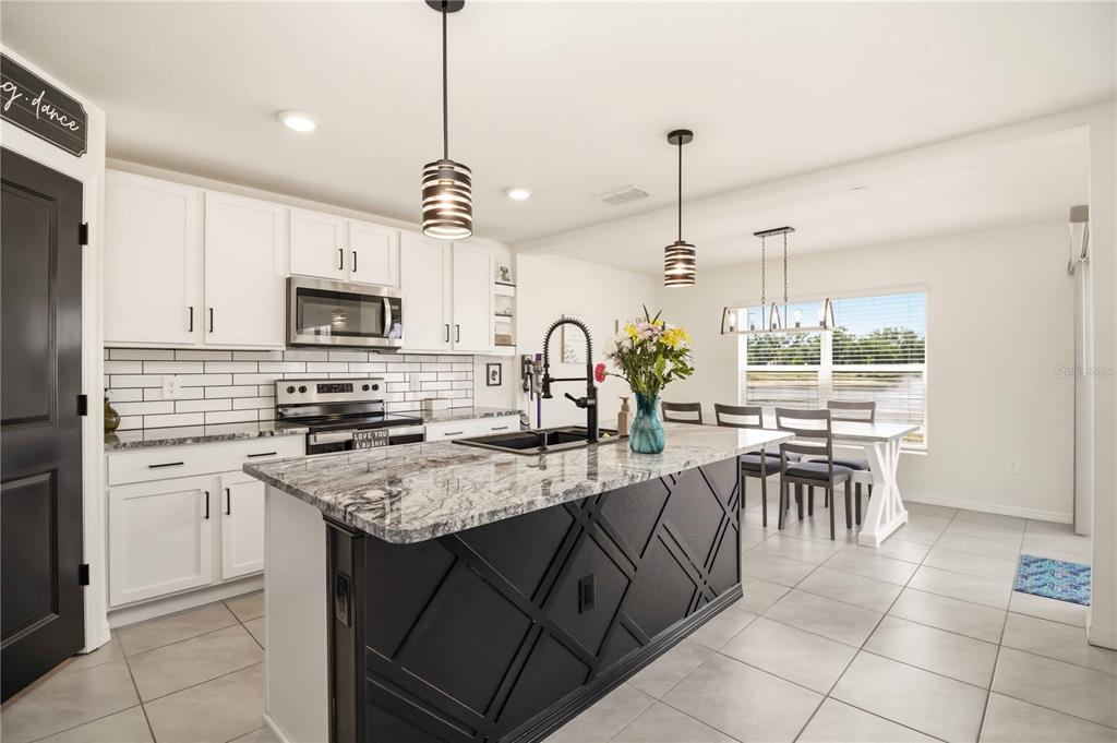A kitchen features white cabinets, a black island with patterned detailing, and a dining area — 2922 ROCK SOUND STREET, BRADENTON, FL