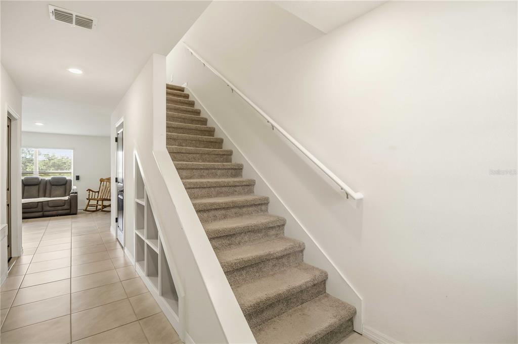 A carpeted staircase with a white handrail sits beside built-in shelving in a tiled hallway — 2922 ROCK SOUND STREET, BRADENTON, FL