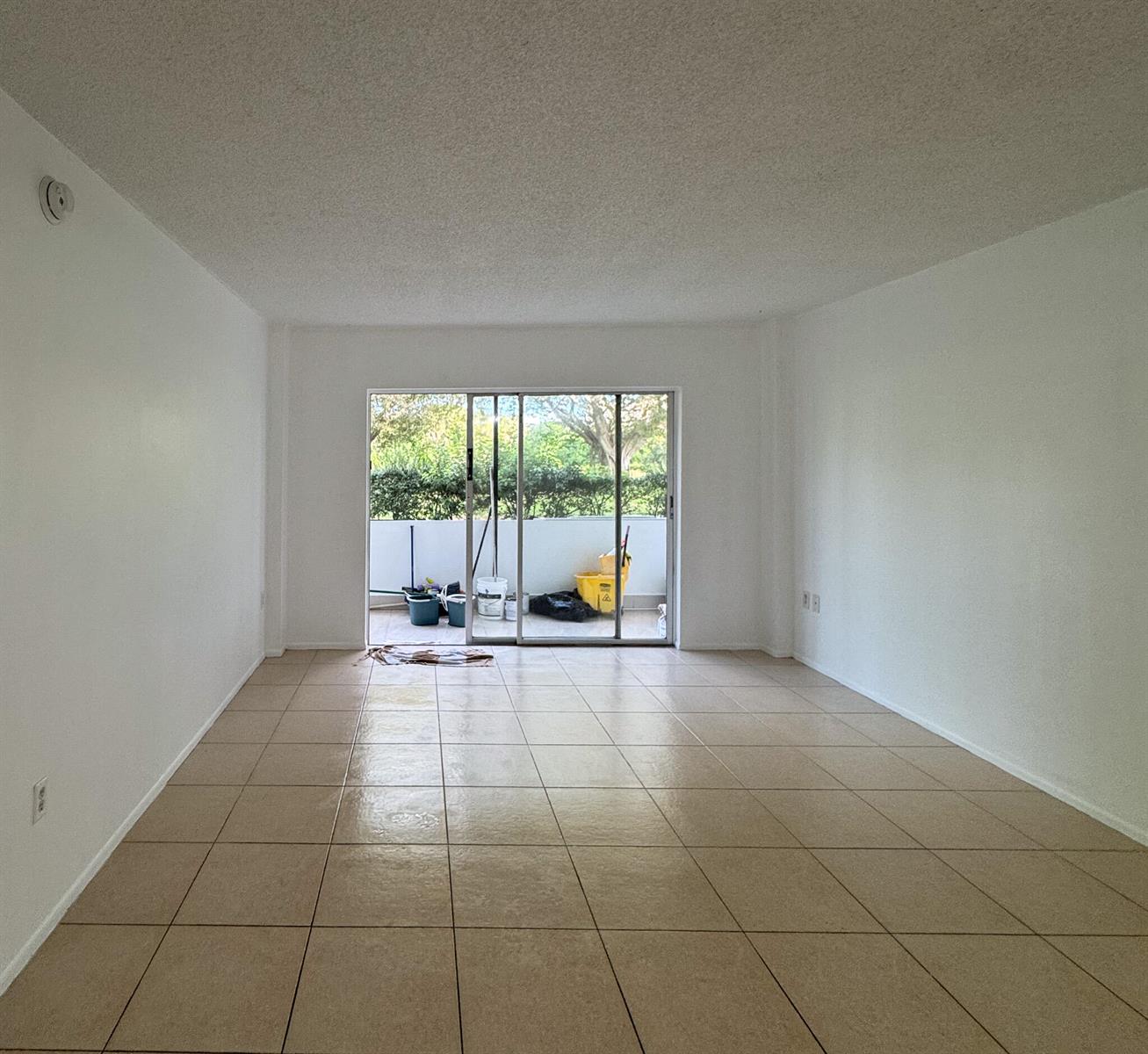 An empty room with white walls, tan tile flooring, and a sliding glass door to a balcony — 4166 Inverrary Drive # 104, Lauderhill FL 33319, LAUDERHILL, FL