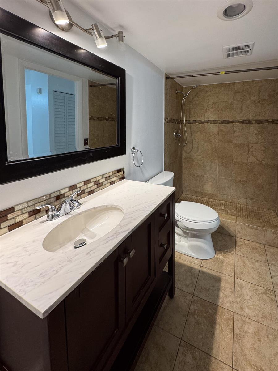 A bathroom features a dark wood vanity, marble-look countertop, and a tiled walk-in shower — 4166 Inverrary Drive # 104, Lauderhill FL 33319, LAUDERHILL, FL