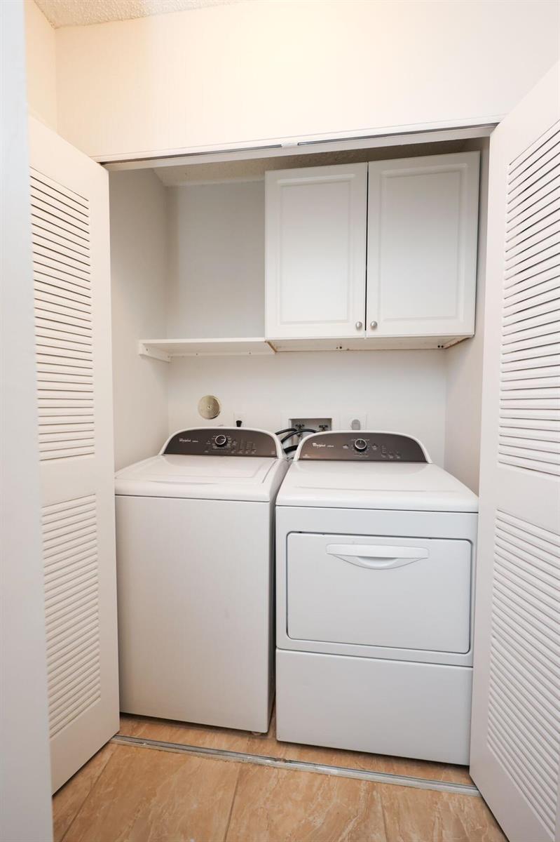 A laundry closet contains a white washer and dryer beneath wall-mounted cabinets and a shelf — 10127 E Boca Bend E # B2, Boca Raton FL 33428, BOCA RATON, FL