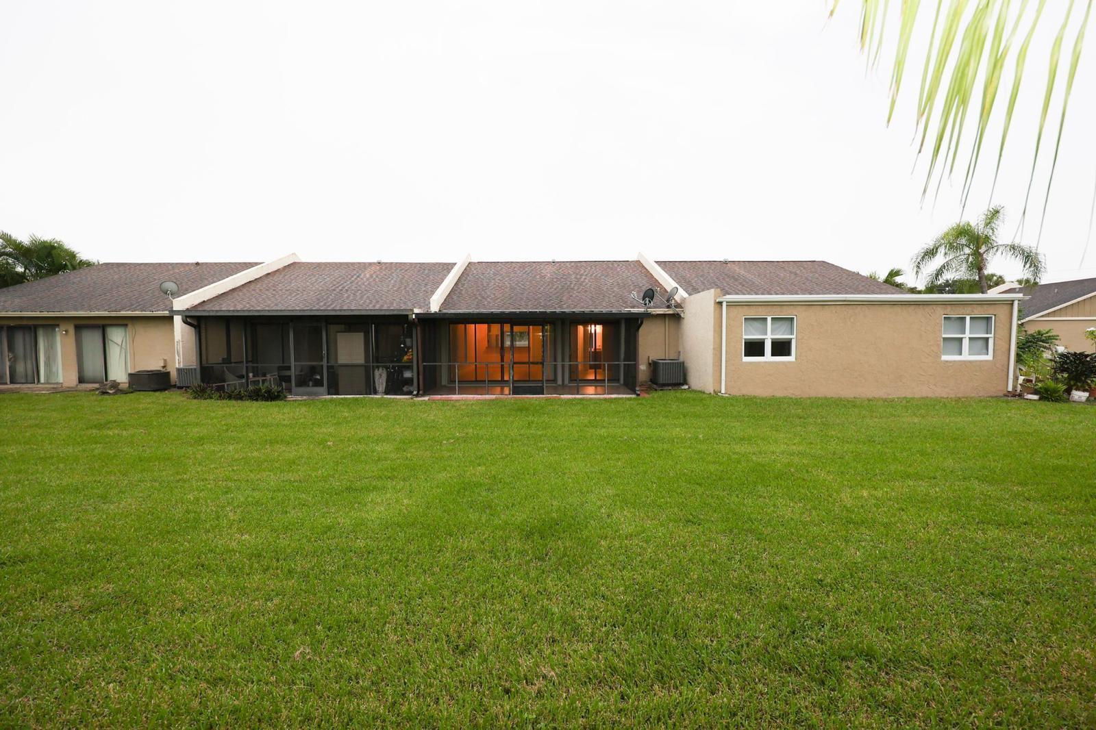 The rear exterior of a single-story home features a screened-in patio and a grassy lawn — 10127 E Boca Bend E # B2, Boca Raton FL 33428, BOCA RATON, FL