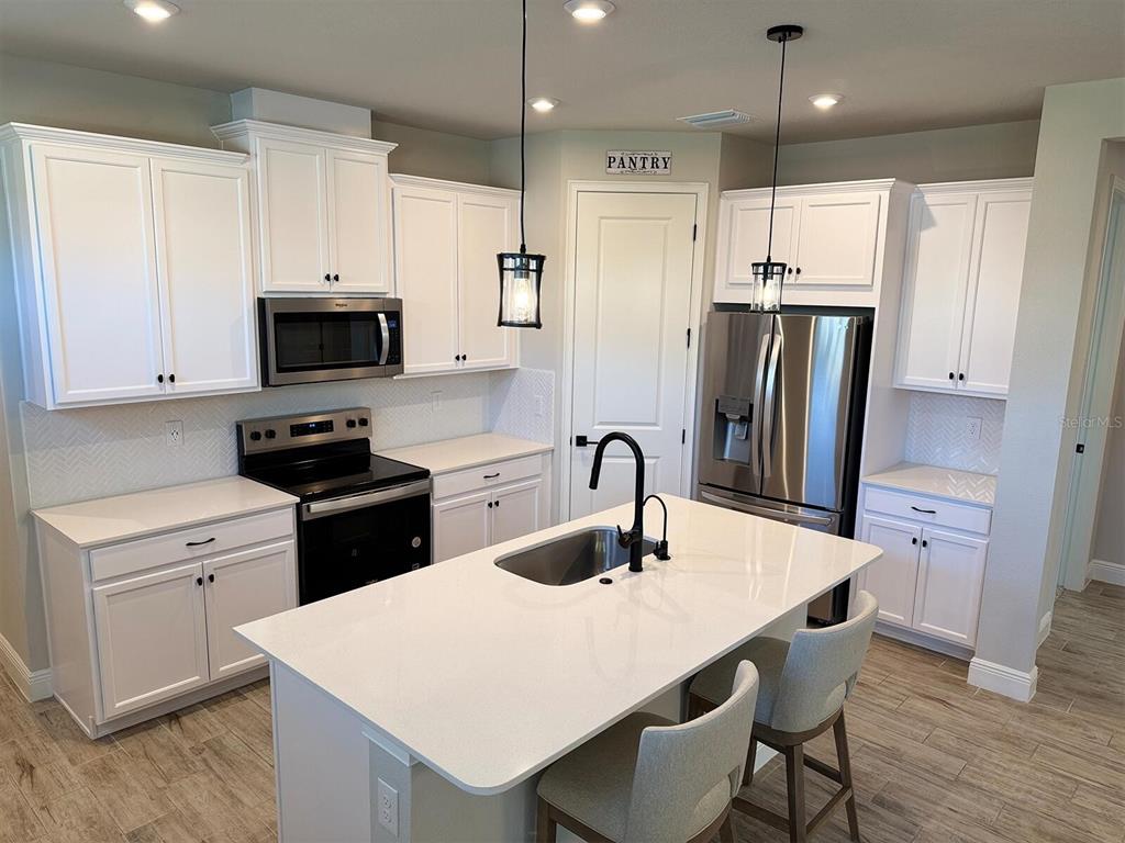 A modern kitchen features white cabinets, stainless steel appliances, a center island, and pendant lighting — 31969 ASBURY AVENUE, WESLEY CHAPEL, FL
