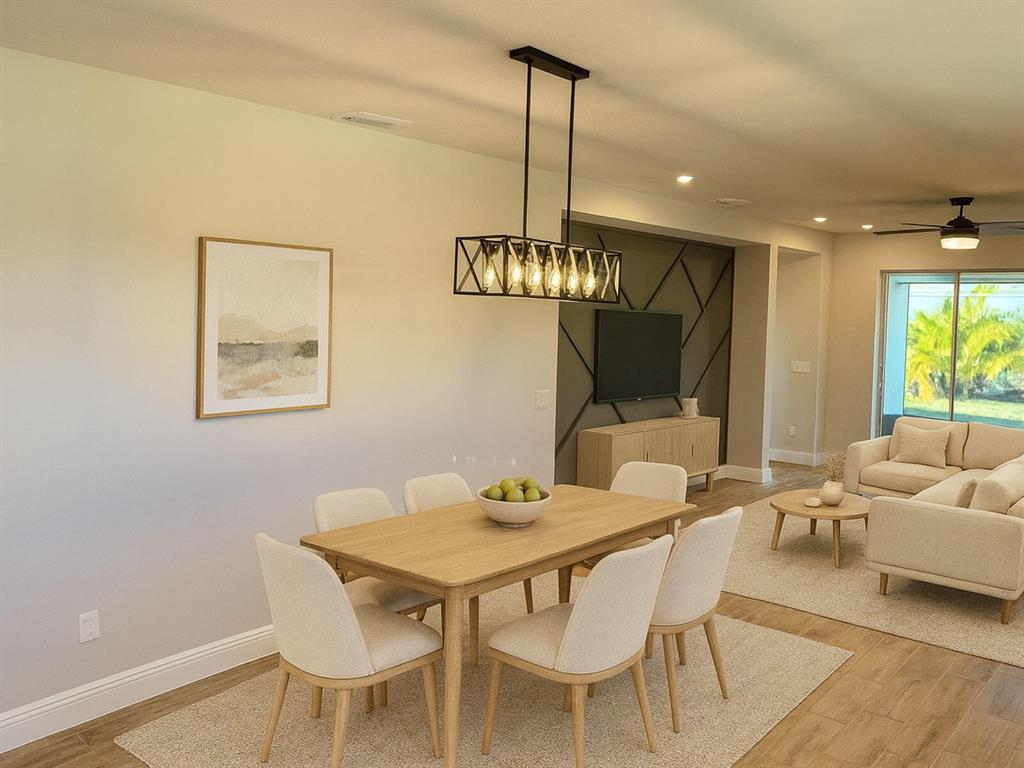 A dining area with a rectangular wooden table and light-colored chairs sits near a living room — 31969 ASBURY AVENUE, WESLEY CHAPEL, FL