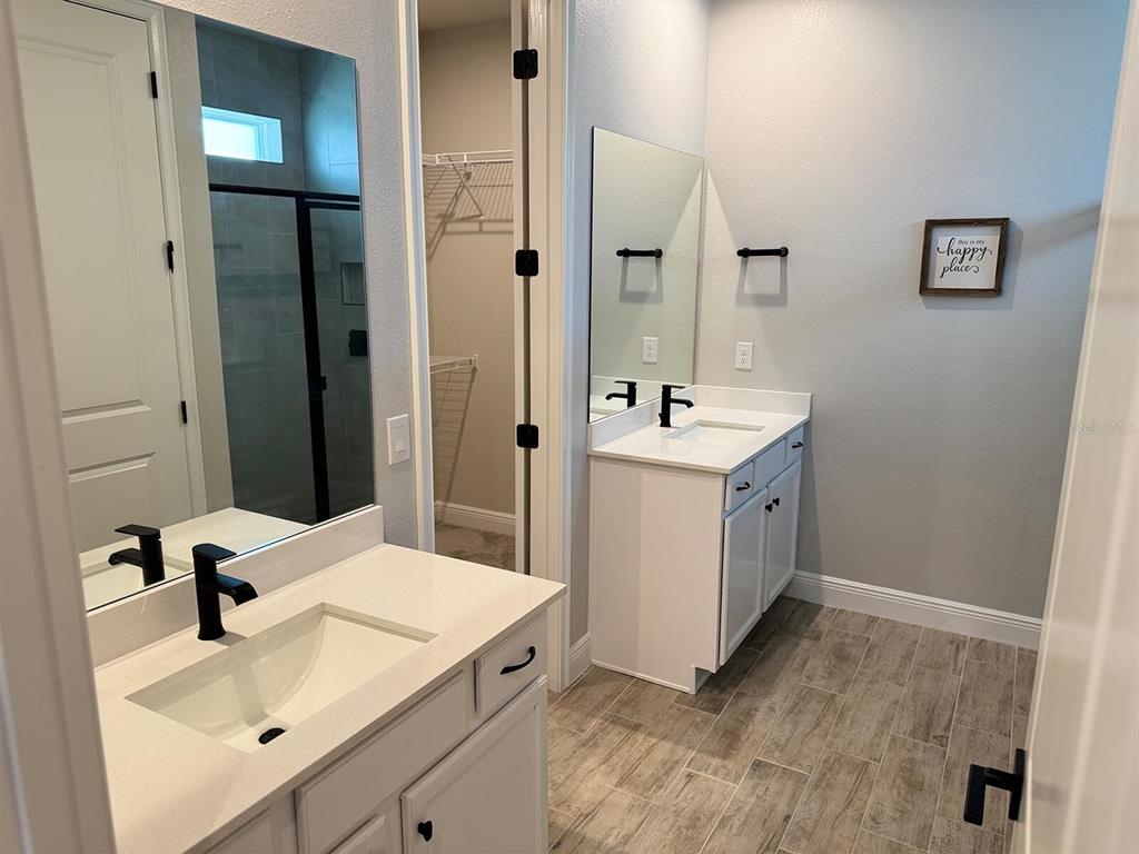 A bathroom features dual white vanities with black faucets, tiled flooring, and an adjacent walk-in closet — 31969 ASBURY AVENUE, WESLEY CHAPEL, FL