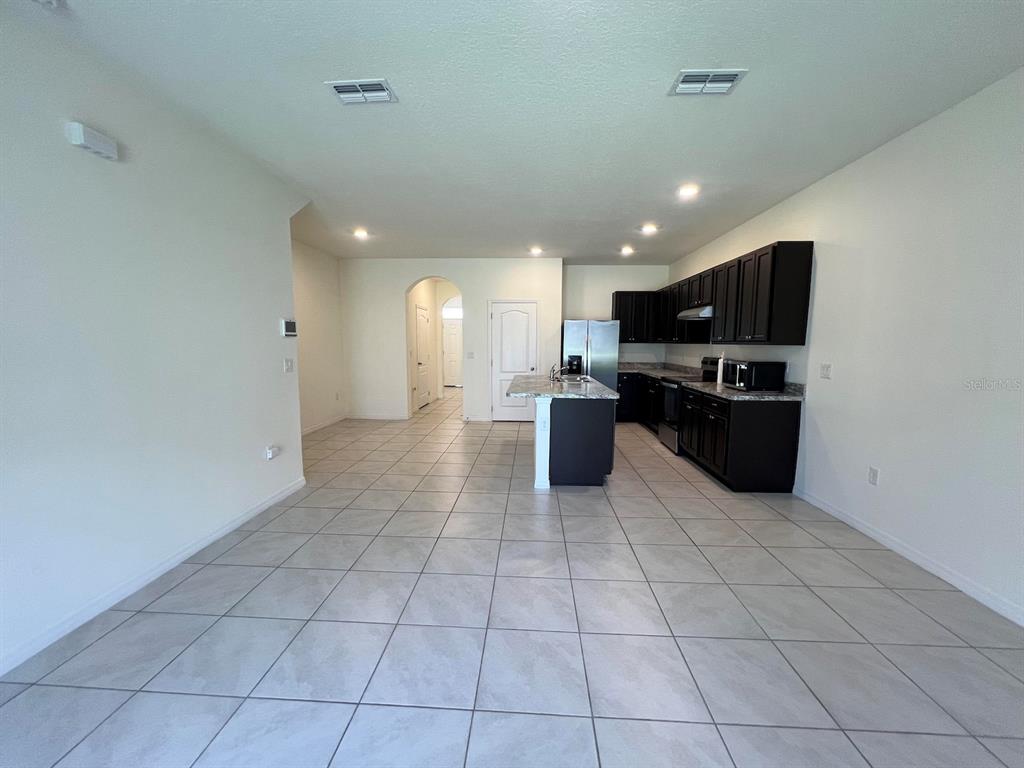 A kitchen with dark cabinets and a central island opens into a tiled living area — 1370 YELLOW FINCH DRIVE, DAVENPORT, FL