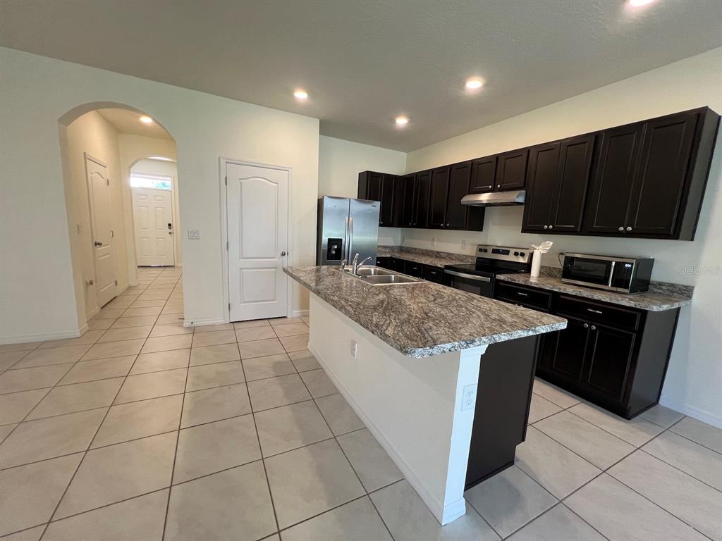 A kitchen features dark wood cabinets, granite countertops, a center island, and tile flooring — 1370 YELLOW FINCH DRIVE, DAVENPORT, FL