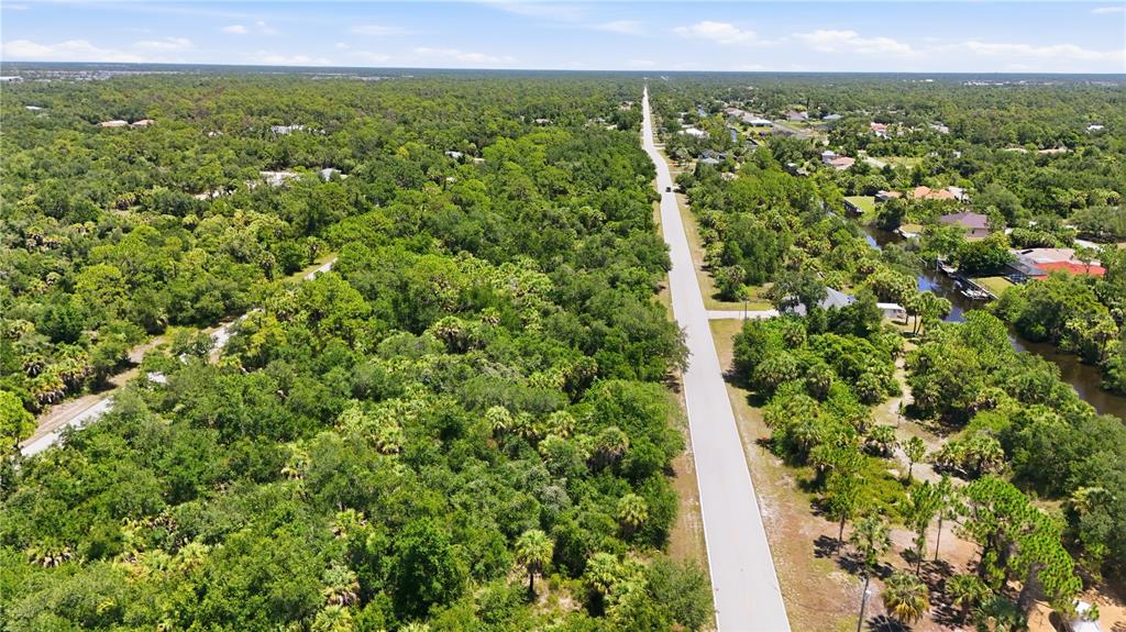 An aerial view shows a paved road running through a dense, wooded residential area — 3139 COMO STREET, PORT CHARLOTTE, FL