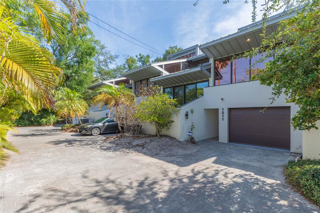 A modern multi-level home with a garage, paved driveway, and large windows under a sunny sky — 1511 S BAY VILLA PLACE, TAMPA, FL