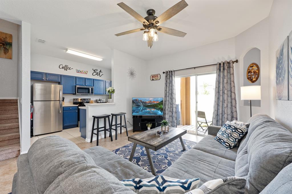 A living room with a grey sectional sofa, coffee table, and an open kitchen with blue cabinets — 2714 CALABRIA AVENUE, DAVENPORT, FL
