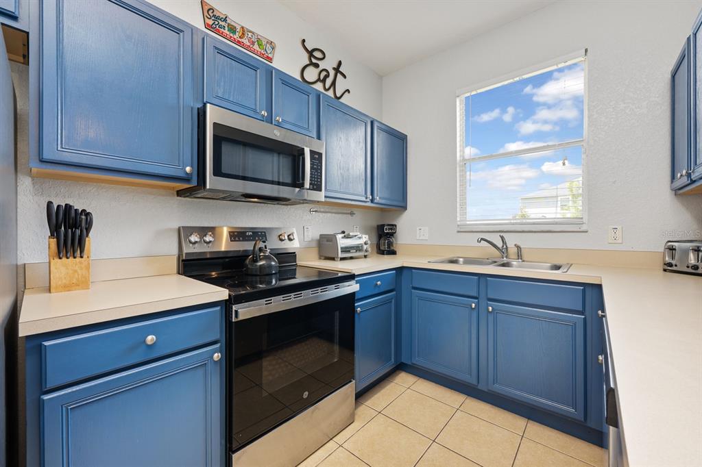 A kitchen features blue cabinets, stainless steel appliances, and beige countertops with tile flooring — 2714 CALABRIA AVENUE, DAVENPORT, FL