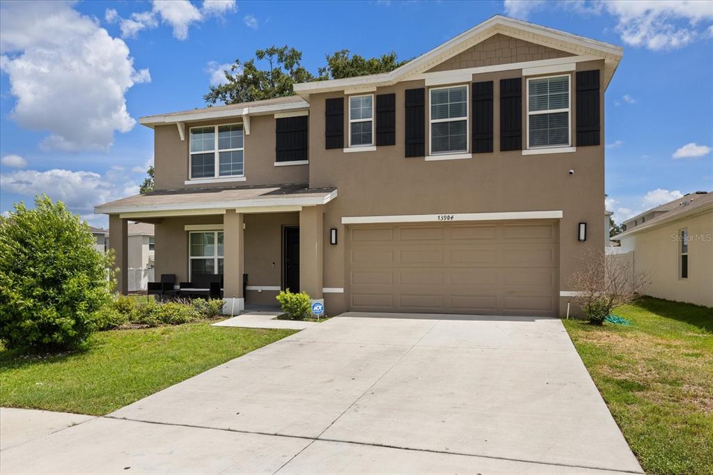 A two-story suburban house with a tan stucco exterior, a two-car garage, and shutters — 13904 WINEBERRY DRIVE, DADE CITY, FL