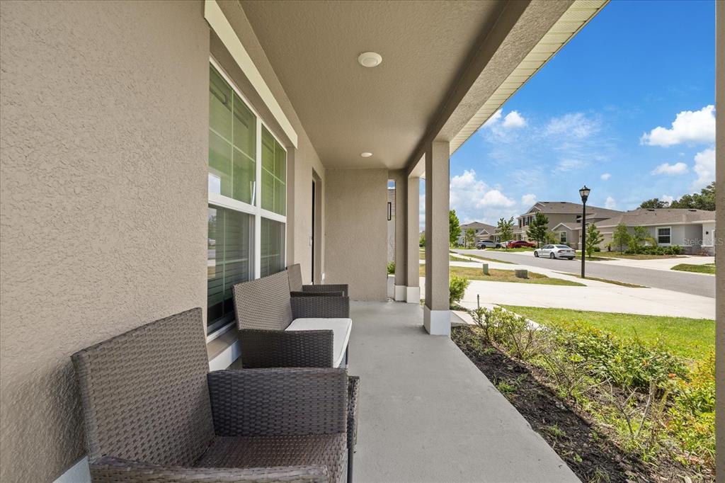 A covered front porch features wicker furniture and a view of a suburban street — 13904 WINEBERRY DRIVE, DADE CITY, FL