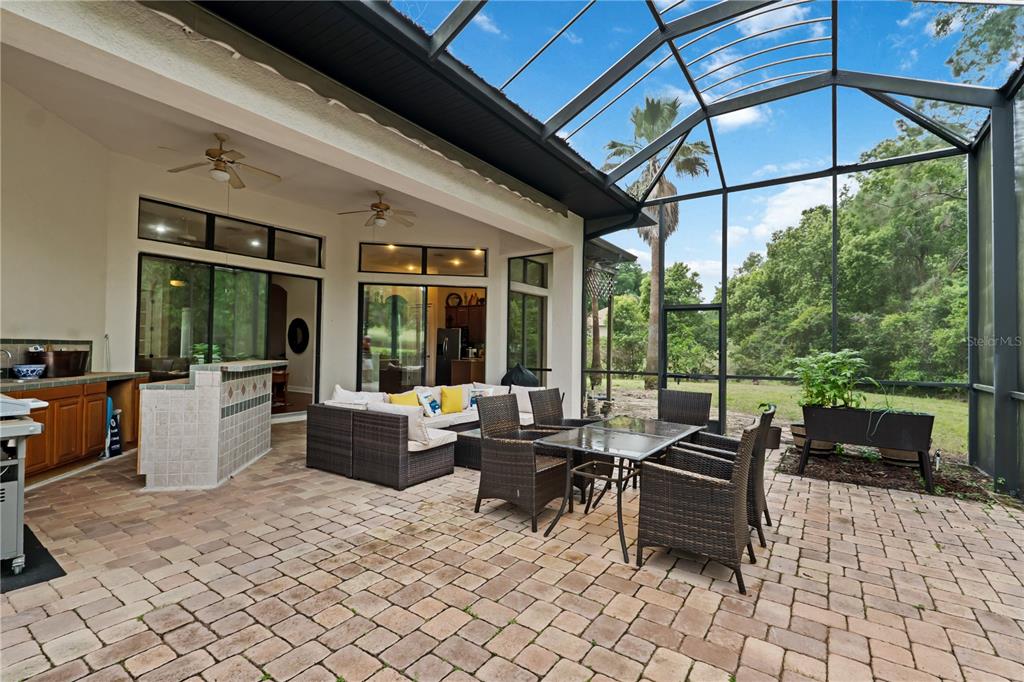 A covered patio features a brick paver floor, outdoor furniture, and a screened-in enclosure — 5204 GREENS DRIVE, LADY LAKE, FL