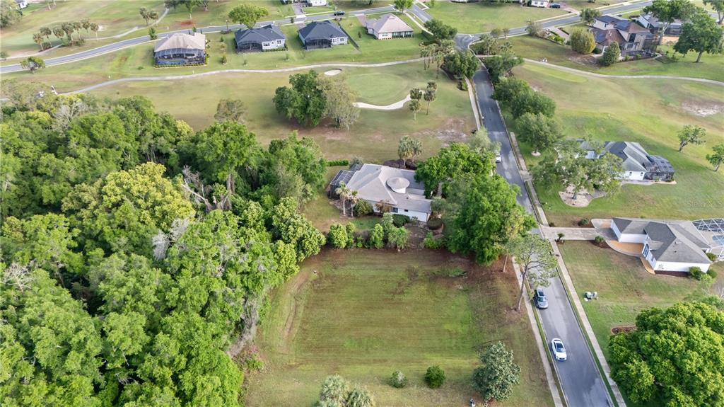 An aerial view shows a vacant residential lot situated between a house and a wooded area — 5204 GREENS DRIVE, LADY LAKE, FL
