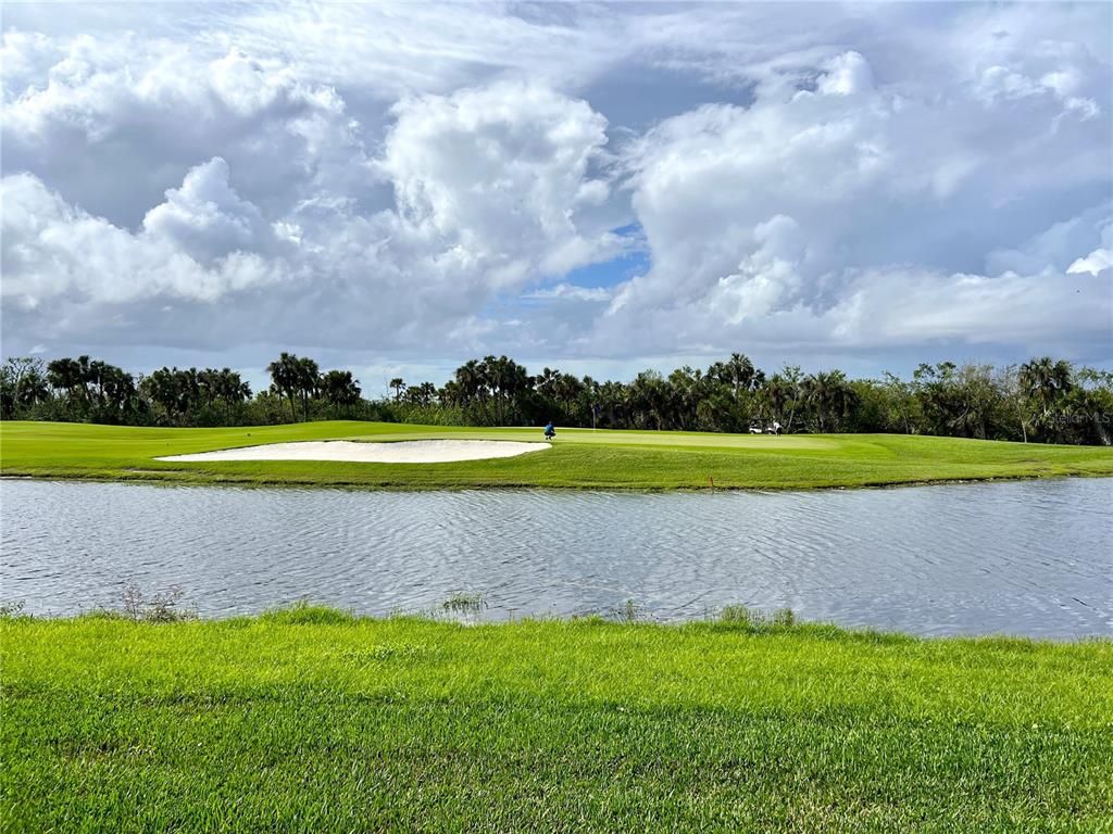 A golf course green with a sand bunker sits across a pond under a cloudy sky — 14061 HERITAGE LANDING BOULEVARD UNIT 434, PUNTA GORDA, FL