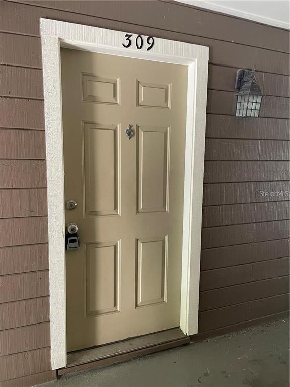 A tan six-panel door with a lockbox and a wall-mounted light fixture on brown siding — 216 AFTON SQUARE UNIT 309, ALTAMONTE SPRINGS, FL