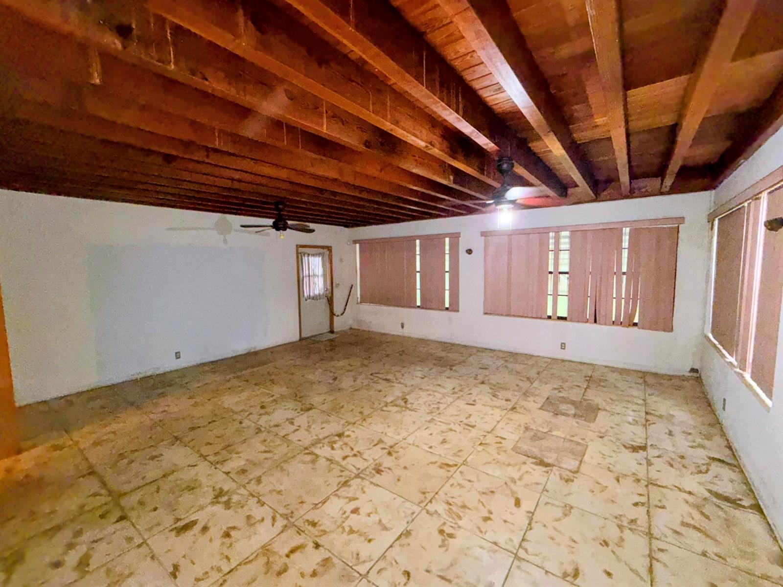 An empty room features a wood-beamed ceiling, tiled flooring, and multiple windows with vertical blinds — 424 NE 72nd Street, Miami FL 33138, MIAMI, FL