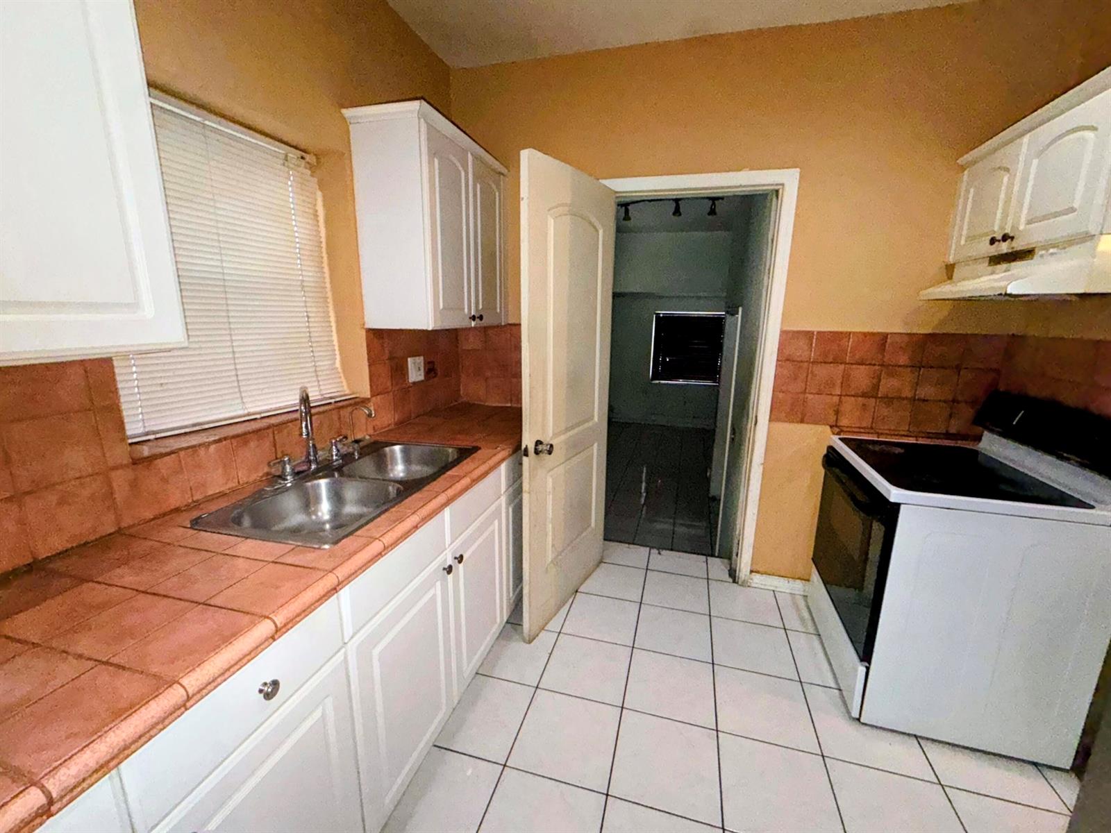 A kitchen features white cabinets, a double sink, tiled countertops, and a white stove — 424 NE 72nd Street, Miami FL 33138, MIAMI, FL