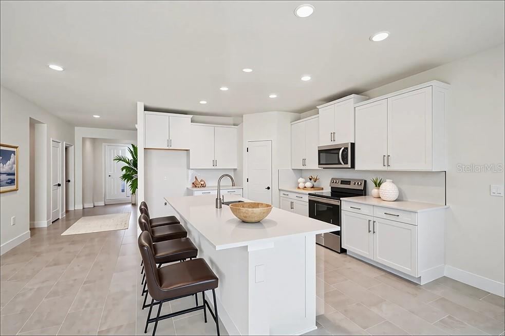 A modern kitchen features white cabinetry, a central island with bar seating, and tile flooring — 17035 NW 180TH TERRACE, ALACHUA, FL