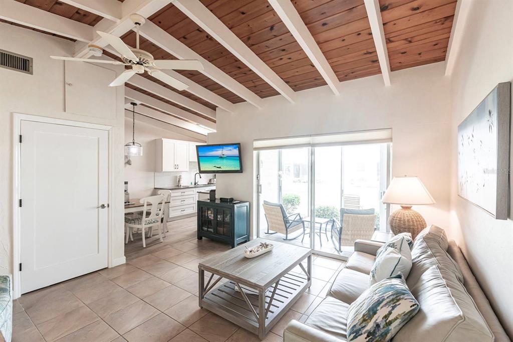 A living room with a wood-beamed ceiling, tile floors, and an adjacent kitchen area — 6006 MIDNIGHT PASS ROAD UNIT 63, SARASOTA, FL