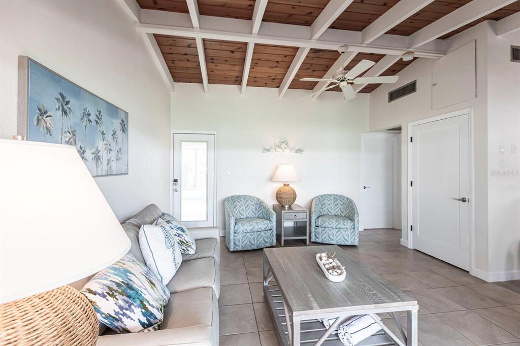 A living room features a vaulted wood-beam ceiling, tile floors, a sofa, and two armchairs — 6006 MIDNIGHT PASS ROAD UNIT 63, SARASOTA, FL