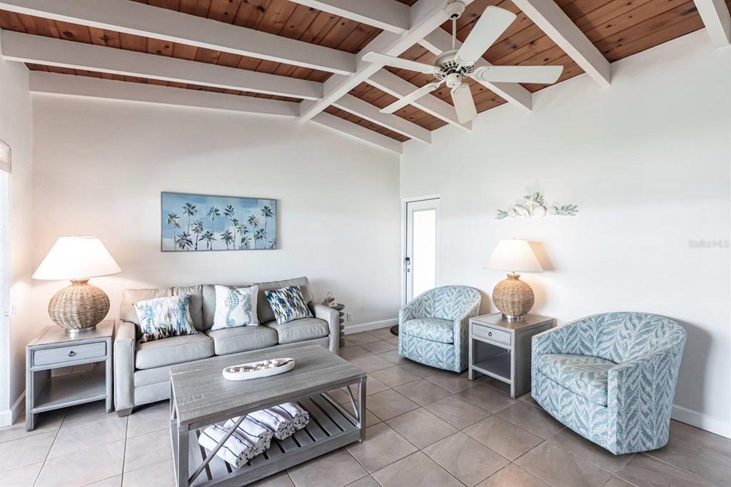 A living room features a vaulted wood-beam ceiling, tile flooring, and coastal-style furniture — 6006 MIDNIGHT PASS ROAD UNIT 63, SARASOTA, FL