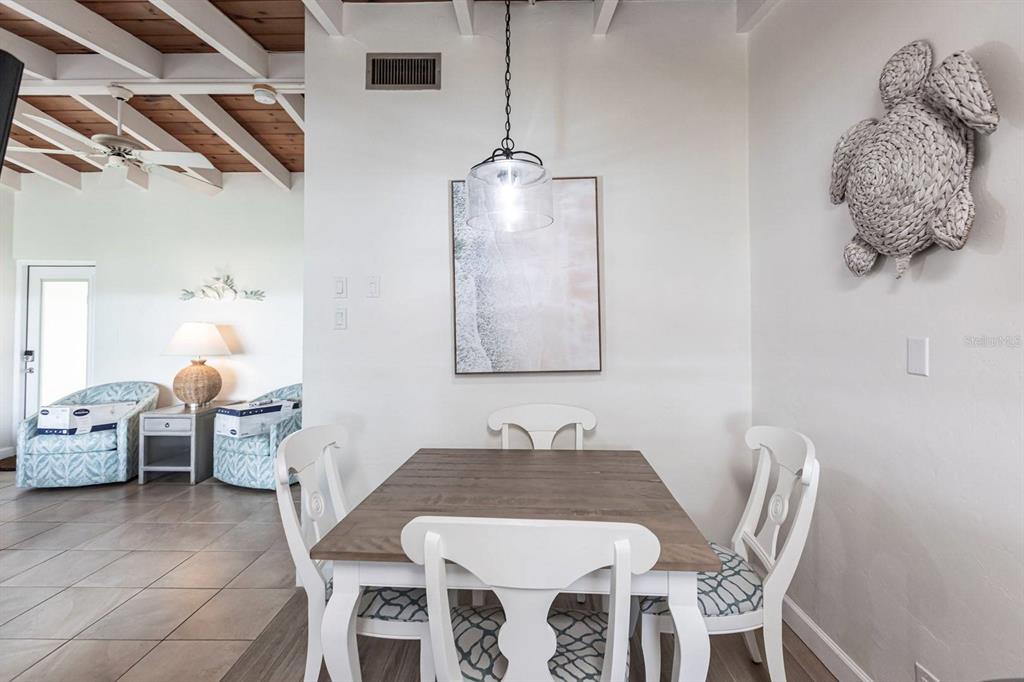 A dining area features a wooden table, four white chairs, and a woven turtle wall decoration — 6006 MIDNIGHT PASS ROAD UNIT 63, SARASOTA, FL