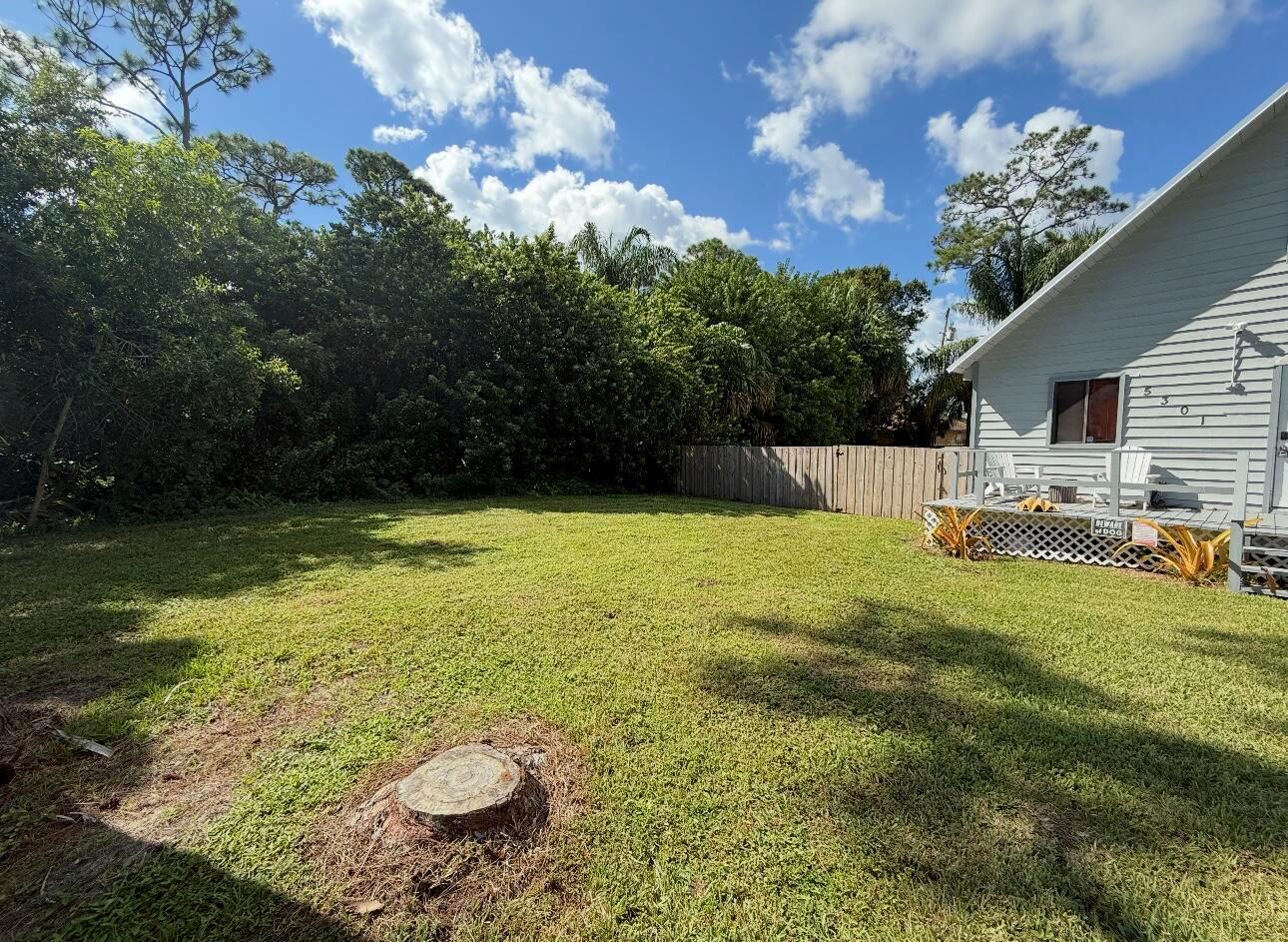 A grassy backyard features a tree stump, a wooden fence, and a house with a deck — 5301 Sunset Boulevard, Fort Pierce FL 34982, FORT PIERCE, FL