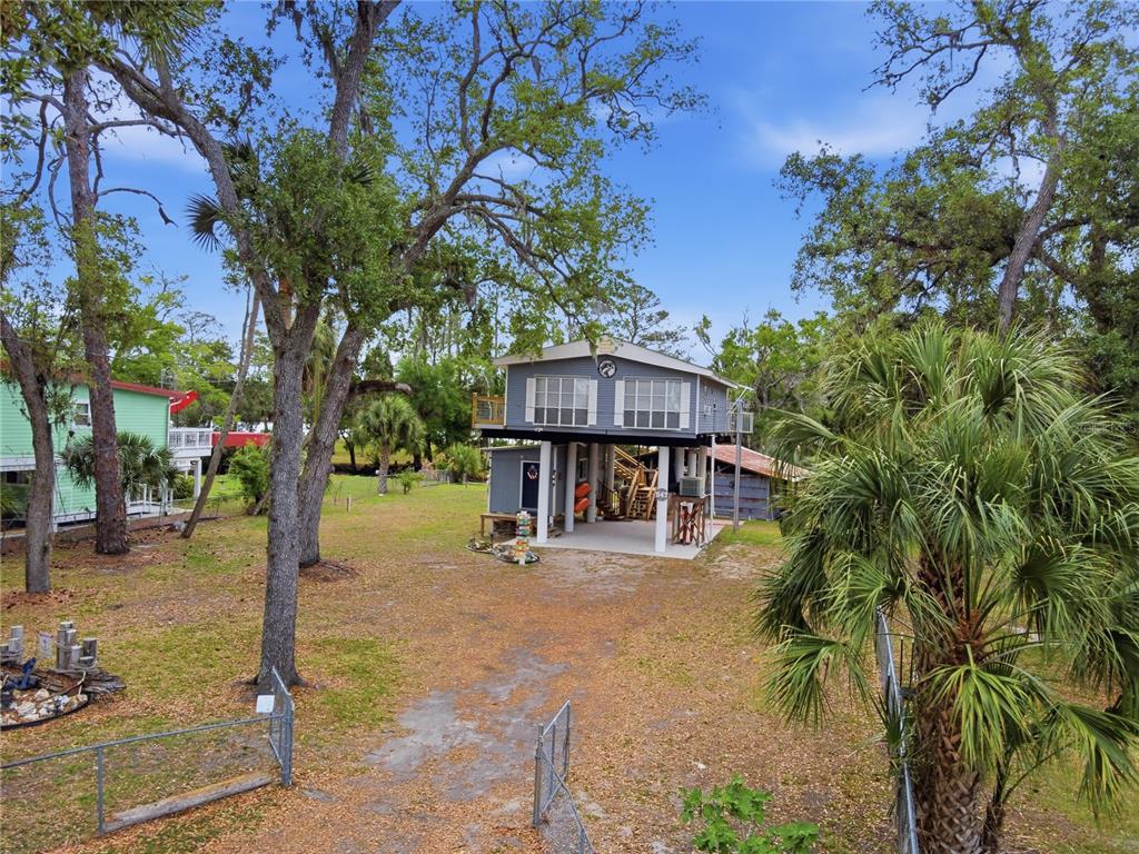 A two-story house on stilts stands in a wooded yard with a chain-link fence — 547 SE 205TH STREET, SUWANNEE, FL