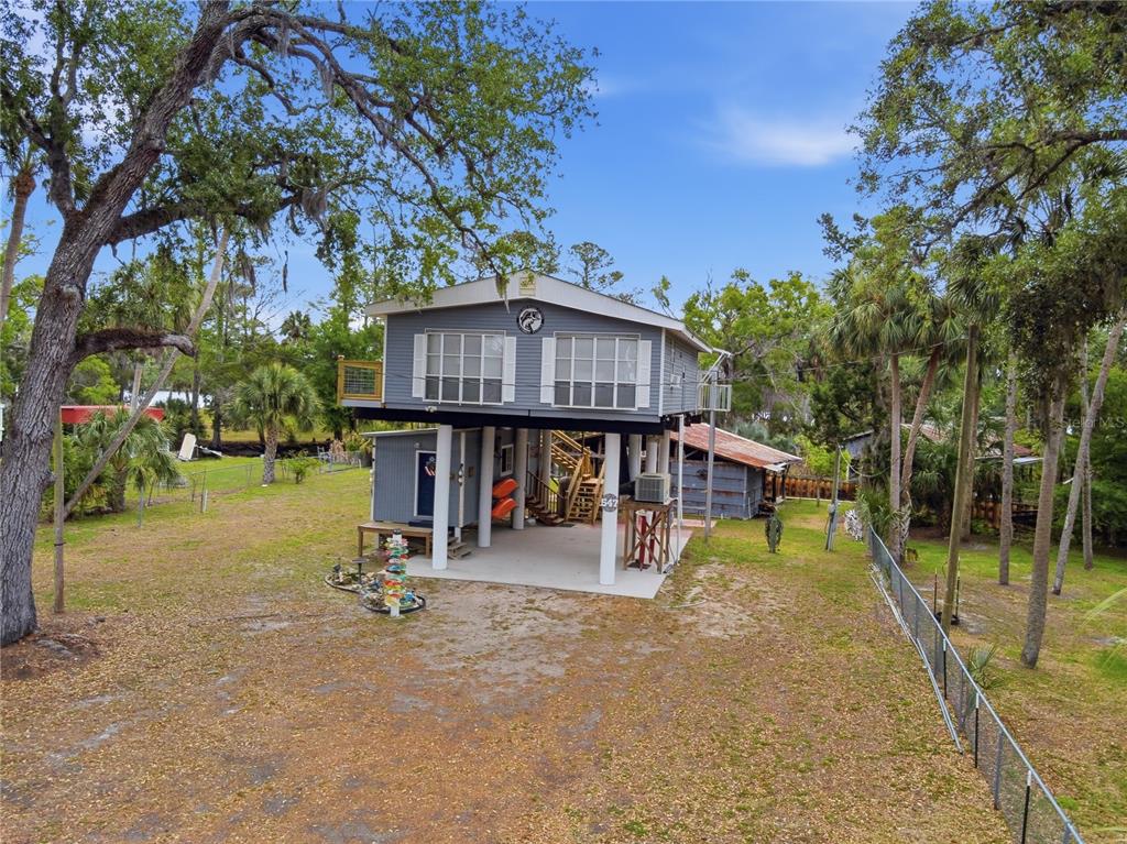 A two-story house elevated on stilts sits on a grassy lot with mature trees — 547 SE 205TH STREET, SUWANNEE, FL