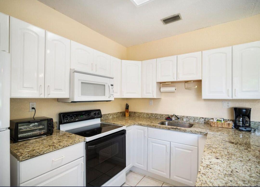 A kitchen features white cabinets, granite countertops, a black stove, and a stainless steel sink — 14870 Horseshoe Trace, Wellington FL 33414, WELLINGTON, FL
