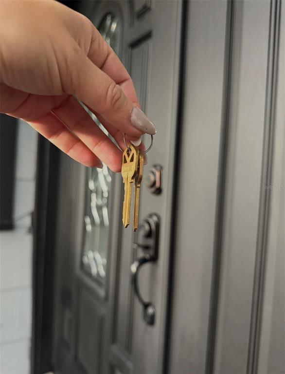A hand holds a set of keys in front of a dark-colored front door — 1221 E DR MARTIN LUTHER KING JR BOULEVARD, TAMPA, FL