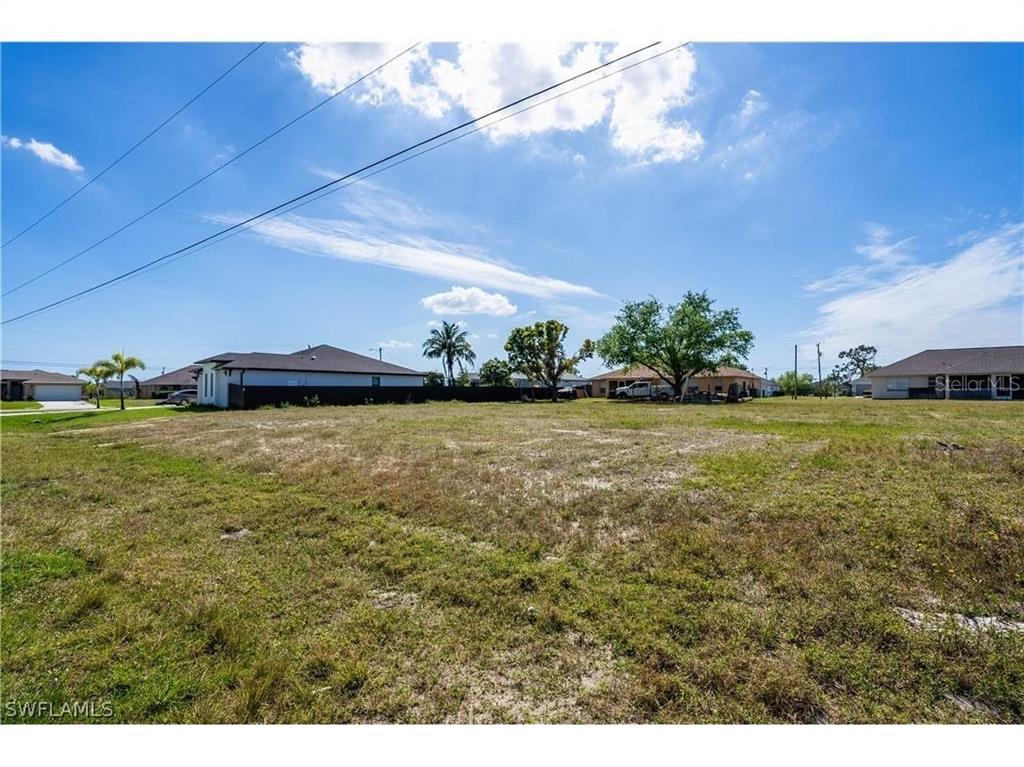 A wide, grassy vacant lot sits under a blue sky with scattered clouds — 33 NW 15TH TERRACE, CAPE CORAL, FL
