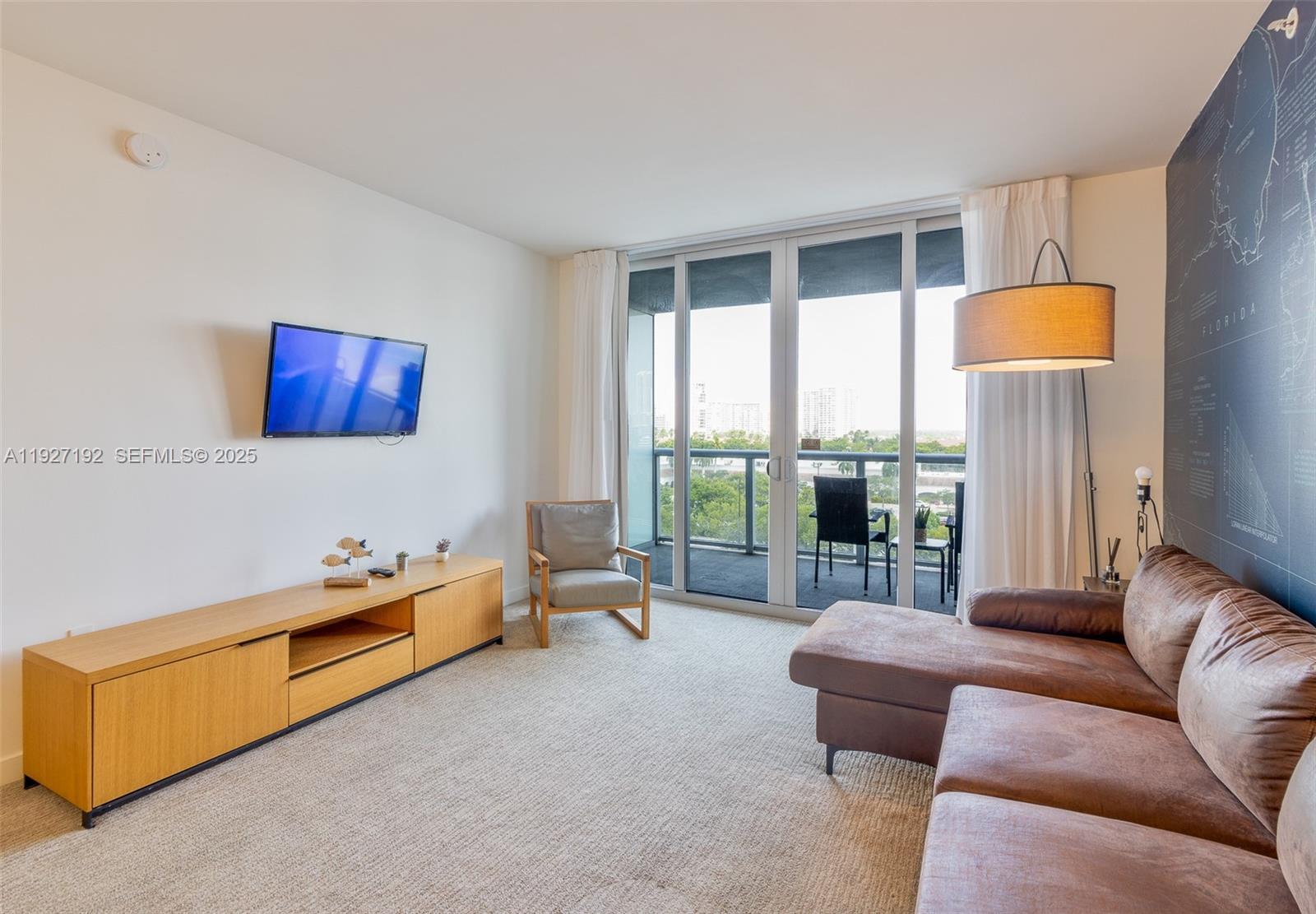 A living room features a brown sectional sofa, a wooden media console, and a balcony view — 2602 E Hallandale Beach Blvd # R708, Hallandale Beach FL 33009, HALLANDALE BEACH, FL