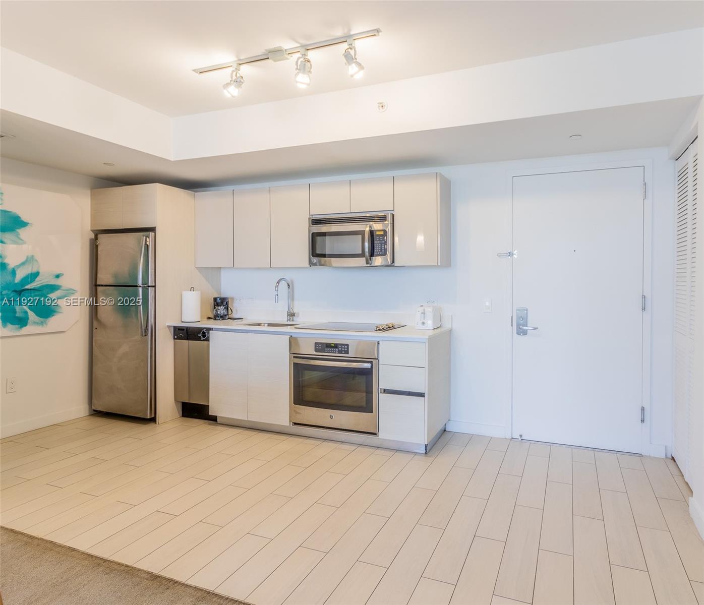 A compact kitchen features light-colored cabinetry, stainless steel appliances, and tile flooring — 2602 E Hallandale Beach Blvd # R708, Hallandale Beach FL 33009, HALLANDALE BEACH, FL