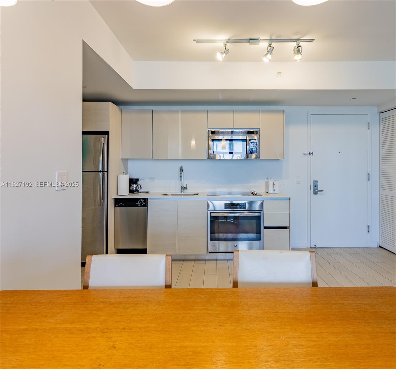 A modern kitchen features light-toned cabinetry, stainless steel appliances, and a wooden dining table — 2602 E Hallandale Beach Blvd # R708, Hallandale Beach FL 33009, HALLANDALE BEACH, FL