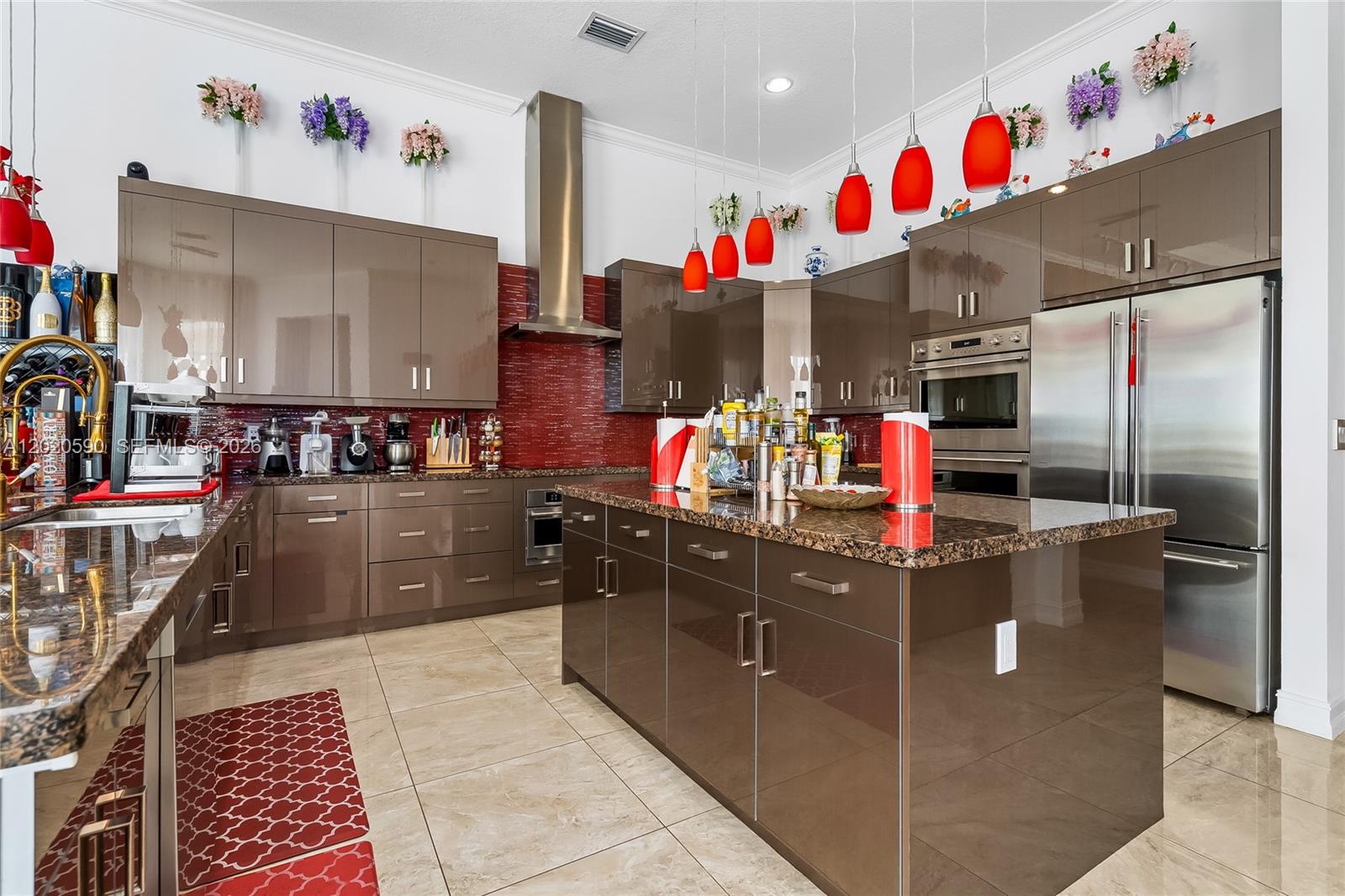 A modern kitchen features glossy brown cabinets, a red tiled backsplash, and a granite island — 5703 N Sterling Ranch Dr, Davie FL 33314, DAVIE, FL