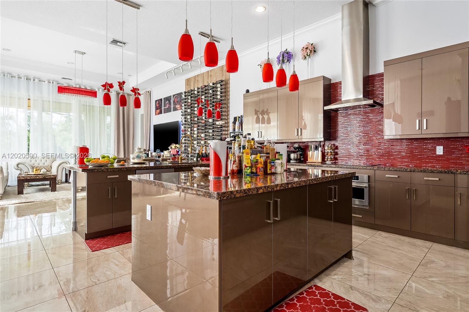 A modern kitchen features two islands, glossy brown cabinets, and a red tiled backsplash — 5703 N Sterling Ranch Dr, Davie FL 33314, DAVIE, FL
