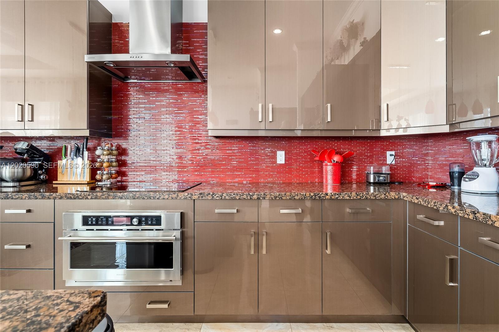 A kitchen features glossy brown cabinets, a red glass tile backsplash, and granite countertops — 5703 N Sterling Ranch Dr, Davie FL 33314, DAVIE, FL