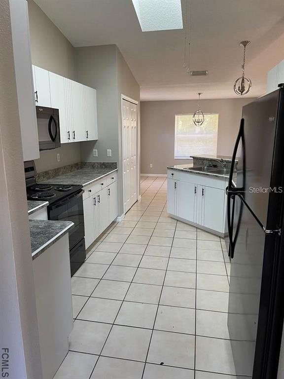 A kitchen features white cabinets, dark countertops, black appliances, and light-colored tile flooring — 61 FRANCISCAN LANE, PALM COAST, FL
